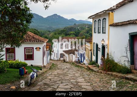 Vista della discesa Rua da Camara strada acciottolata con molte case coloniali su entrambi i lati sotto il cielo nuvoloso nel centro storico di Tiradentes. Foto Stock