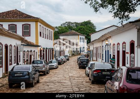 Edifici coloniali fianco a fianco si trova in Direita strada con auto parcheggiate nelle vicinanze nel centro storico di Tiradentes sotto il cielo nuvoloso. Foto Stock