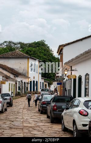 Edifici coloniali fianco a fianco si trova in Direita strada con auto parcheggiate nelle vicinanze nel centro storico di Tiradentes sotto il cielo nuvoloso. Foto Stock