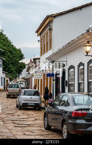 Edifici coloniali fianco a fianco si trova in Direita strada con auto parcheggiate nelle vicinanze nel centro storico di Tiradentes sotto il cielo nuvoloso. Foto Stock