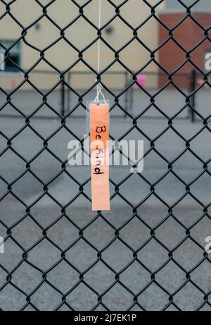 Una scheda laminata della nota (sia genere)è appesa da una recinzione di collegamento della catena in un cortile della scuola, che rappresenta anti bullismo, Ontario, Canada - fotografia di riserva Foto Stock
