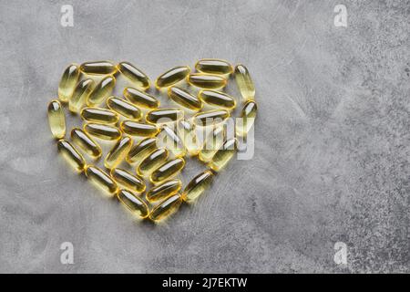 Capsule a forma di cuore omega-3 su sfondo grigio. Il concetto di medicina e di vita sana. Vista dall'alto. Foto Stock