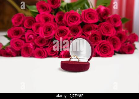 Anello d'oro in una confezione regalo rossa e un grande bouquet di rose sullo sfondo. Foto Stock