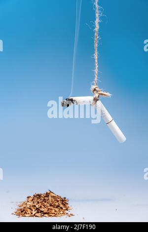 Giornata mondiale del controllo del tabacco. La sigaretta fumante è appesa su un mucchio di tabacco su sfondo blu. Spazio di copia. Verticale. Il concetto di nicotina addictio Foto Stock