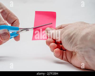 Uomo che taglia carta artigianale rosa con forbici blu a sinistra fuoco selezionato Foto Stock