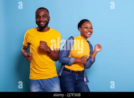 La coppia afroamericana che fa danza si muove insieme in studio, sentendosi allegra e spensierata. Gente felice che balla al ritmo e sorride davanti alla macchina fotografica, divertendosi in relazione. Foto Stock