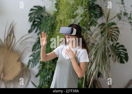 Intrattenimento virtuale nel giardino di casa. Donna gioita in visore VR che gioca a un videogioco interattivo Foto Stock