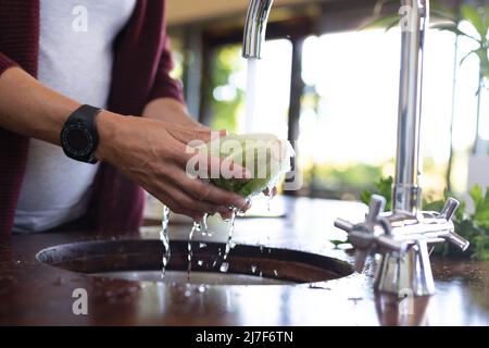 Metà sezione di donna incinta caucasica che lava le verdure nel lavandino in cucina a casa Foto Stock