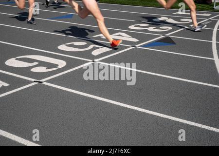 Pista all'aperto e corsa in campo su una pista grigia con corsie numerate e una linea di arrivo con spazio di riproduzione. Due guide attraversano la linea. Foto Stock