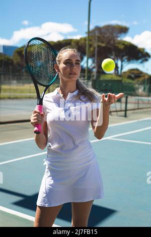 Bella tennista caucasica giovane donna in piedi con racchetta e palla in campo in giorno di sole Foto Stock