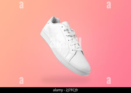Vista ad angolo alto della sneaker bianca isolata su sfondo peachy. Scarpe sportive per mockup. Scarpe sportive casual alla moda. Foto Stock