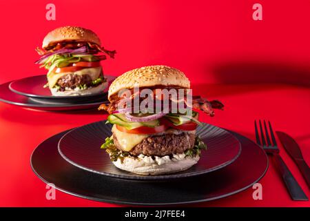 Cheeseburger fresco con lattuga, cetriolo, pomodoro, cipolla e pancetta su sfondo rosso vibrante Foto Stock