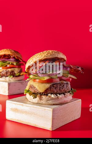 Cheeseburger fresco con lattuga, cetriolo, pomodoro, cipolla e pancetta su sfondo rosso vibrante Foto Stock