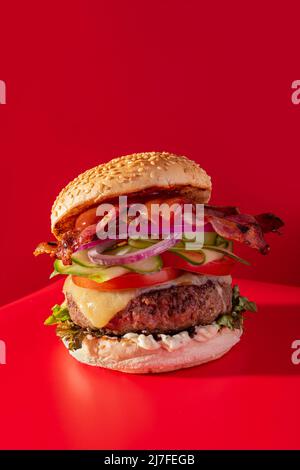 Cheeseburger fresco con lattuga, cetriolo, pomodoro, cipolla e pancetta su sfondo rosso vibrante Foto Stock