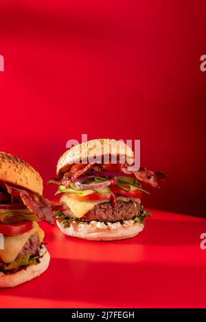 Cheeseburger fresco con lattuga, cetriolo, pomodoro, cipolla e pancetta su sfondo rosso vibrante Foto Stock