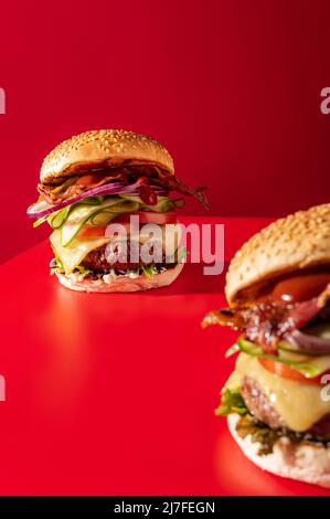 Cheeseburger fresco con lattuga, cetriolo, pomodoro, cipolla e pancetta su sfondo rosso vibrante Foto Stock