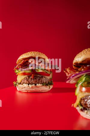 Cheeseburger fresco con lattuga, cetriolo, pomodoro, cipolla e pancetta su sfondo rosso vibrante Foto Stock