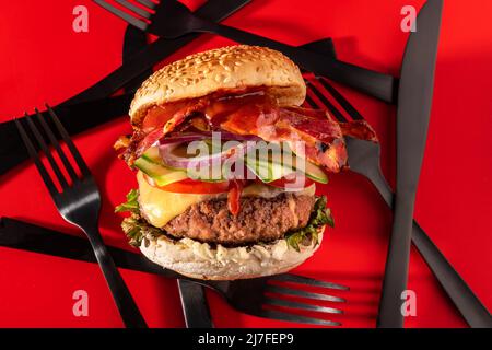 Cheeseburger fresco con lattuga, cetriolo, pomodoro, cipolla e pancetta su sfondo rosso vibrante Foto Stock