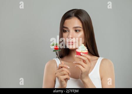 Concetto di cibo malsano e sano. Bella donna con dolci e verdure Foto Stock
