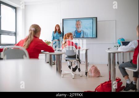 Vista posteriore del gruppo di ragazzi della scuola seduti e ascoltando l'insegnante in aula Foto Stock
