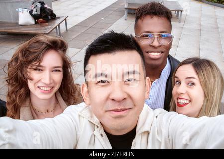 Da sopra l'uomo asiatico sorridendo e prendendo selfie con amici multirazziale il giorno del fine settimana in strada Foto Stock