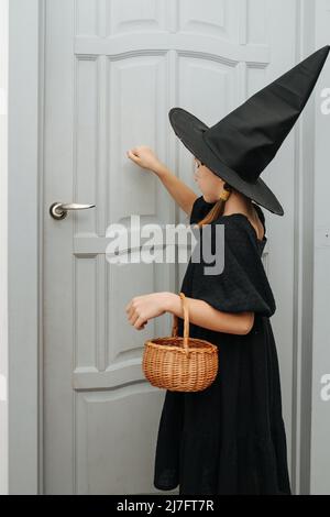 Bambina in costume da strega che bussa alla porta, scherzare o trattare. I suoi occhi chiusi, raccogliendo il suo coraggio. Foto Stock