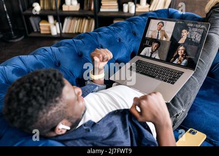 Soddisfatto uomo afroamericano rilassante a divano allenatore con computer portatile sulle gambe, gioioso uomo d'affari freelance studente sognare, riposo dopo il lavoro Foto Stock