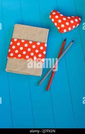 Taccuino vintage, cuore con tessuto a pois rosso e matite in legno su sfondo blu Foto Stock