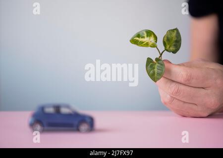 Mano che tiene la foglia, auto giocattolo in background Foto Stock