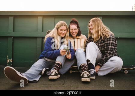 Ragazze adolescenti seduti su skateboard e utilizzando smartphone Foto Stock