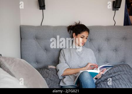 Giovane donna seduta sul divano e libro di lettura Foto Stock