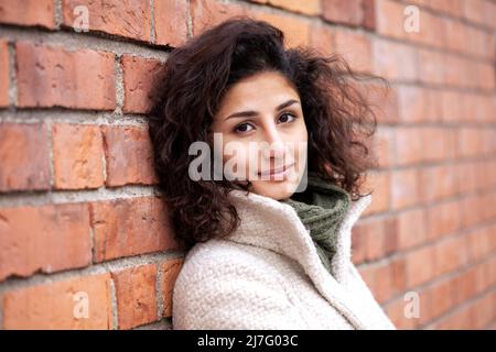 Ritratto di giovane donna appoggiata contro un muro di mattoni Foto Stock