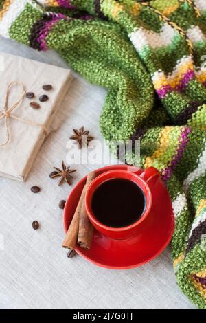 Caffè espresso caldo fresco e delizioso con chicchi di caffè in una tazza rossa e un notebook artigianale su sfondo chiaro. Poi c'è un plaid a strisce luminoso. Foto Stock