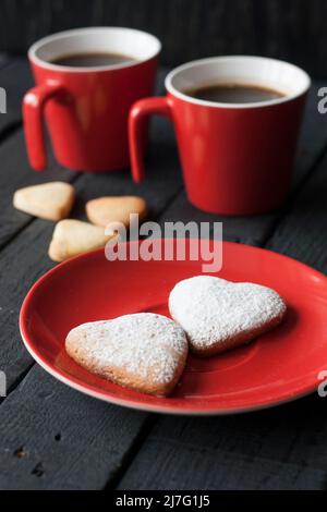 Coppa rossa e biscotti cuori su sfondo nero al giorno di San Valentino Foto Stock