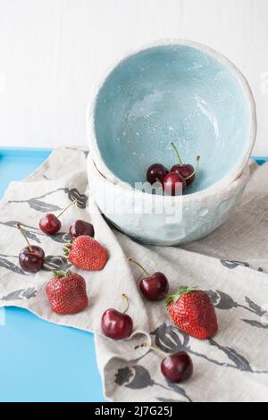 Piatti blu con fragole rosse succose e deliziose ciliegie su sfondo di legno blu Foto Stock