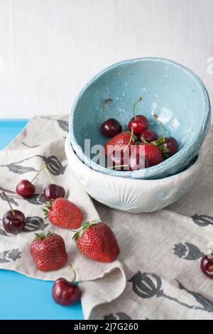 Piatti blu con fragole rosse succose e deliziose ciliegie su sfondo di legno blu Foto Stock