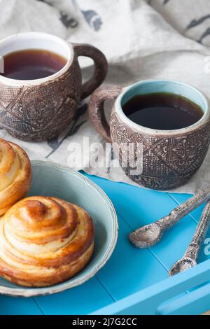 Gustosi panini con marmellata e due tazze di tè su sfondo di legno blu. Poi ci sono due cucchiai e un tovagliolo di lino leggero. Foto Stock