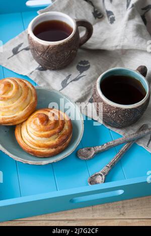 Gustosi panini con marmellata e due tazze di tè su sfondo di legno blu. Poi ci sono due cucchiai e un tovagliolo di lino leggero. Foto Stock