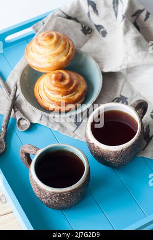 Gustosi panini con marmellata e due tazze di tè su sfondo di legno blu. Poi ci sono due cucchiai e un tovagliolo di lino leggero. Foto Stock