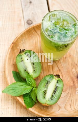 Cocktail con kiwi e basilico in un bicchiere su sfondo di legno. Foto Stock