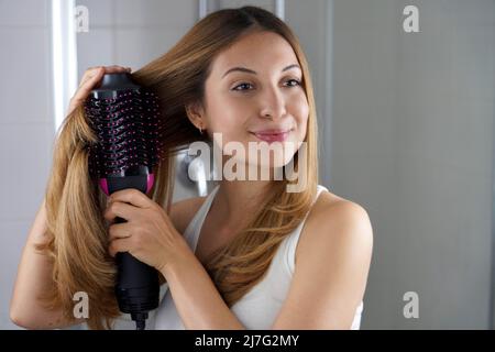 Ragazza con spazzola asciugacapelli per acconciare i capelli allo specchio in bagno Foto Stock