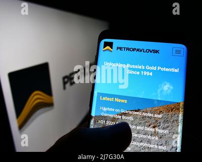 Persona che tiene smartphone con pagina web della società russa di estrazione dell'oro Petropavlovsk plc su schermo con logo. Concentrarsi sul centro del display del telefono. Foto Stock