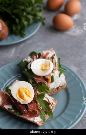 Sandwich con pane integrale, formaggio fatto in casa, rucola, prosciutto e uova. Snack sano. Foto Stock