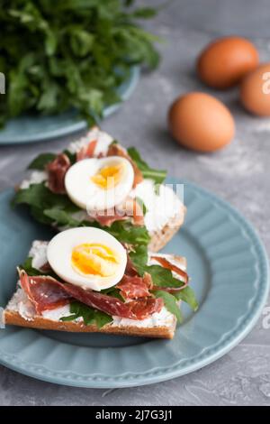 Sandwich con pane integrale, formaggio fatto in casa, rucola, prosciutto e uova. Snack sano. Foto Stock