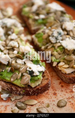 Due grandi sandwich a base di pane senza glutine nero, avocado, formaggio e semi di zucca. Foto Stock