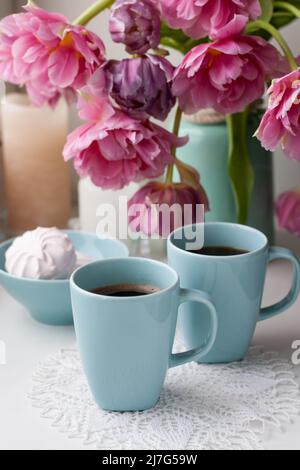 Due tazze di caffè nero e una delicata marshmallow a colazione sono accanto ad un bel bouquet di tulipani rosa in un vaso blu. Foto Stock