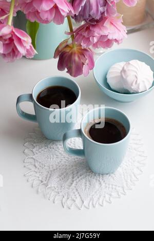 Due tazze di caffè nero e una delicata marshmallow a colazione sono accanto ad un bel bouquet di tulipani rosa in un vaso blu. Foto Stock