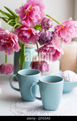 Due tazze di caffè nero e una delicata marshmallow a colazione sono accanto ad un bel bouquet di tulipani rosa in un vaso blu. Foto Stock