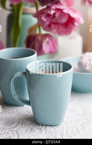 Due tazze di caffè nero e una delicata marshmallow a colazione sono accanto ad un bel bouquet di tulipani rosa in un vaso blu. Foto Stock