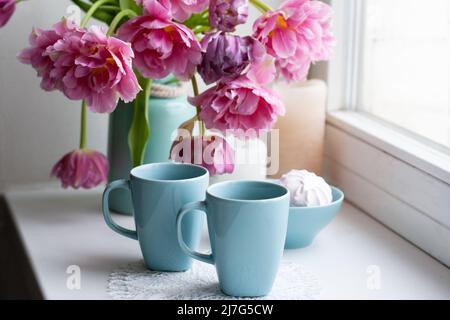 Due tazze di caffè nero e una delicata marshmallow a colazione sono accanto ad un bel bouquet di tulipani rosa in un vaso blu. Foto Stock